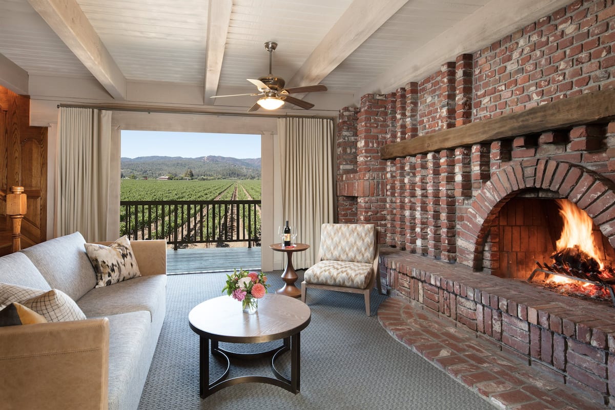 A cozy living room with a brick fireplace, a sofa, a chair, and a table with flowers.