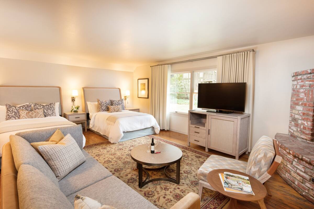 A hotel room with a bed, a sofa, a TV, a coffee table, and a fireplace.