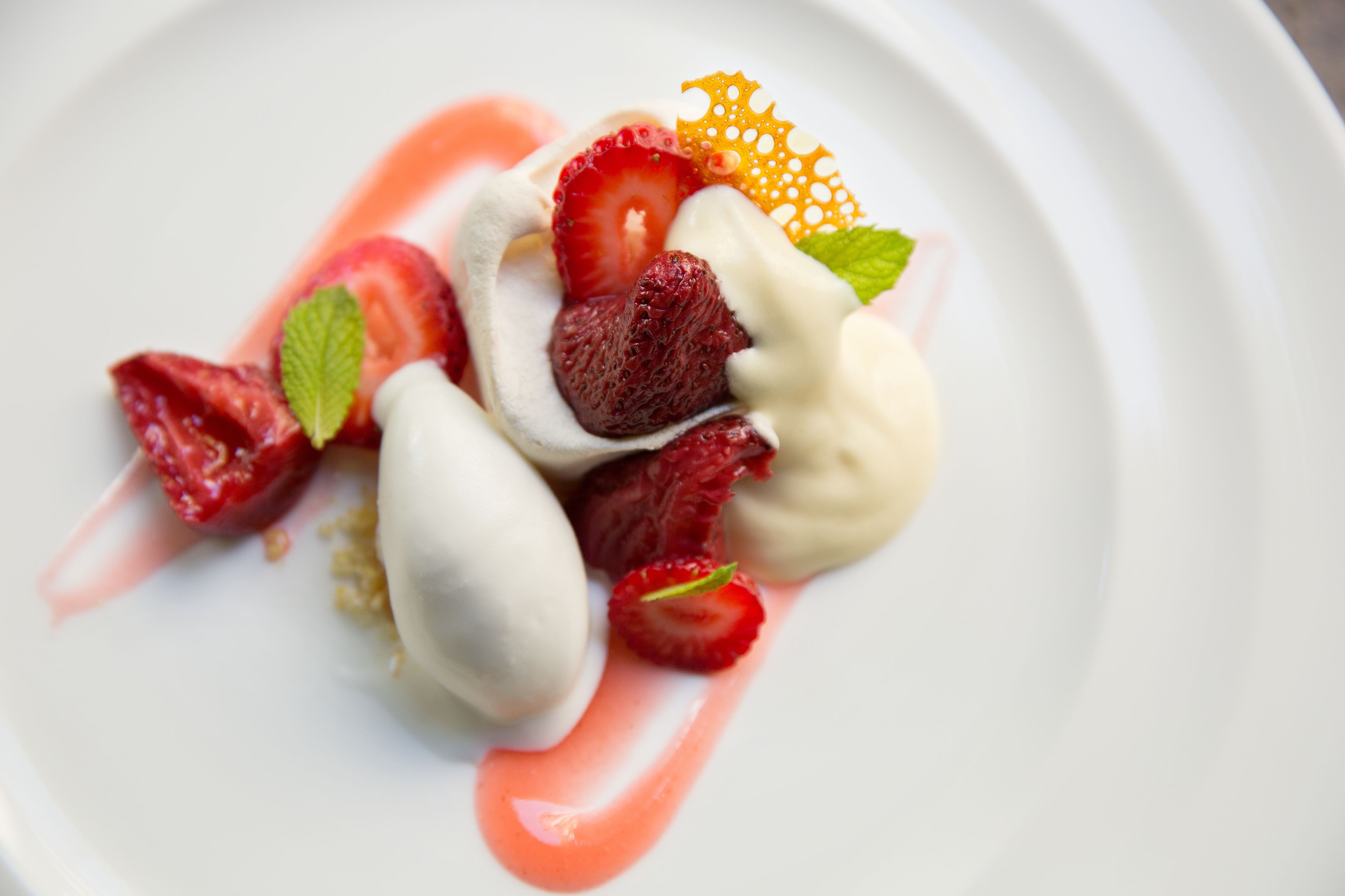 Un plato de postre con fresas, menta y una rodaja de naranja decorativa.
