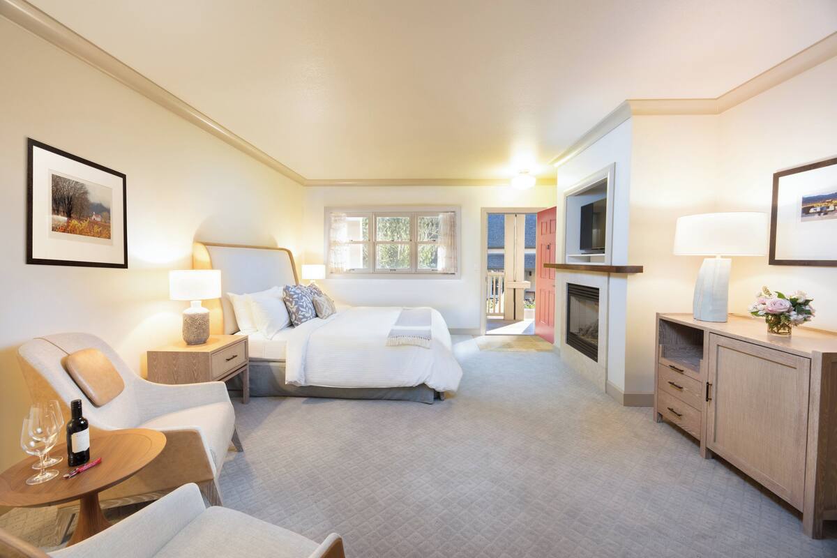 A hotel room with a bed, a desk, a chair, a TV, and a fireplace.