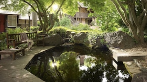 A serene garden with a pond, wooden benches, and a stone pathway leading to a building with a balcony. - Harvest Inn (St. Helena)
