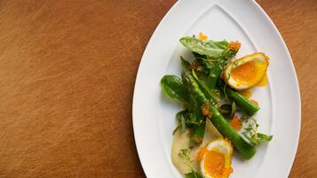 Een witte bord met een salade van bladgroenten, asperges en een gepocheerd ei op een houten tafel.