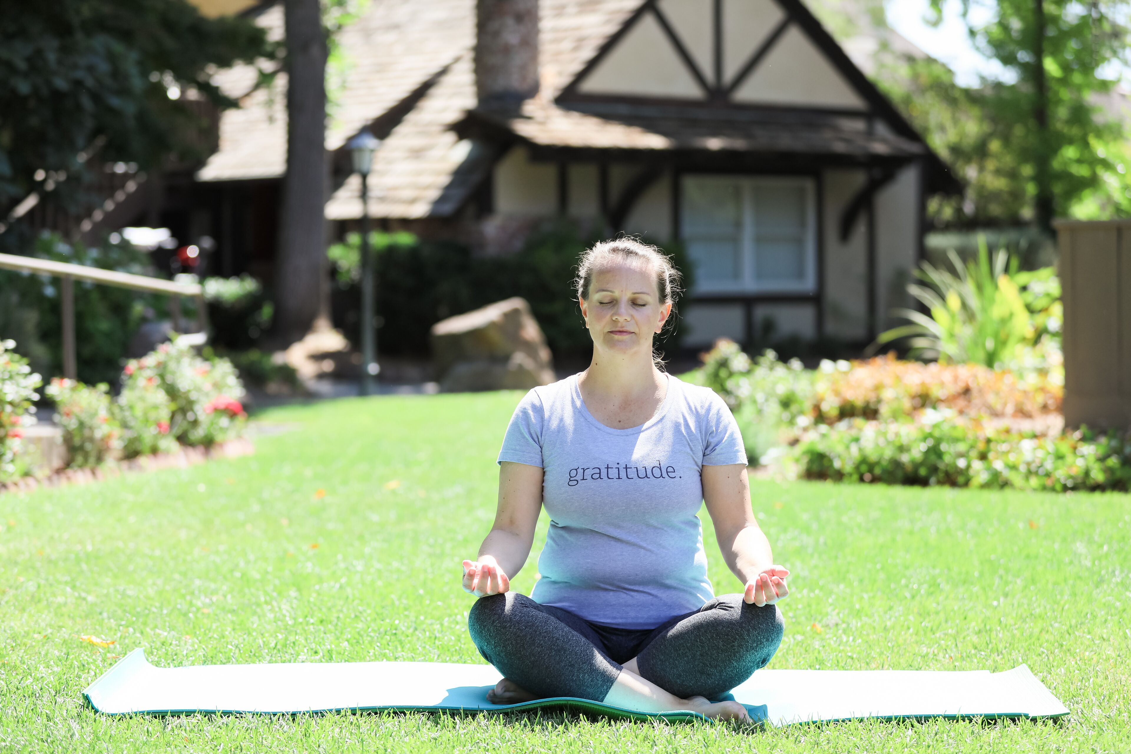 A person sitting on a yoga mat in a grassy area with a house in the background.