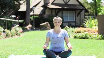 A person sitting on a yoga mat in a grassy area with a house in the background.