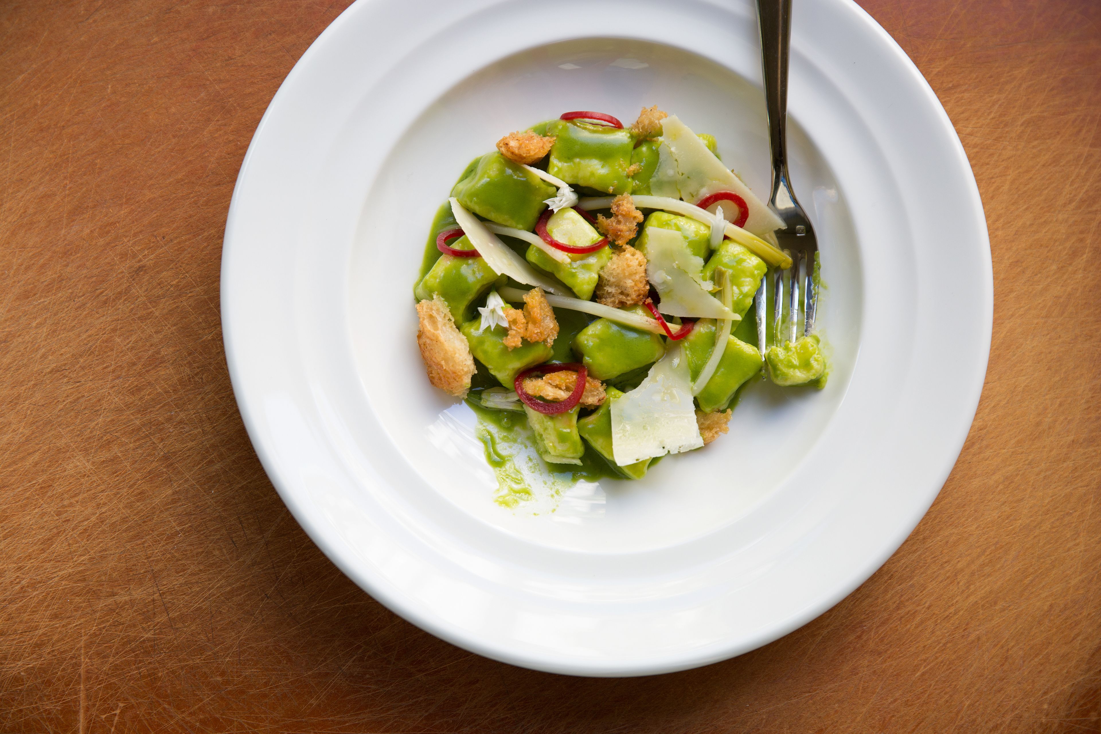 Un plato blanco con una ensalada verde sobre una mesa de madera.