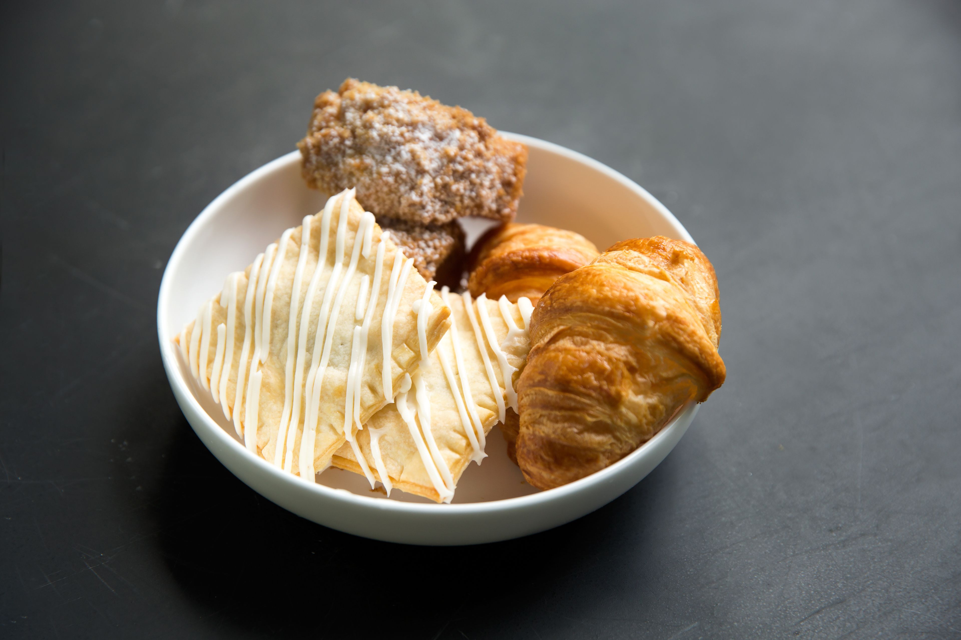 Un tazón con un pastel de cobertura blanca, un croissant y un postre desmenuzado.
