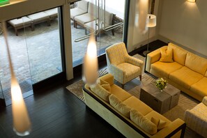 A modern living room with a yellow sofa, patterned armchair, and a coffee table with a vase.