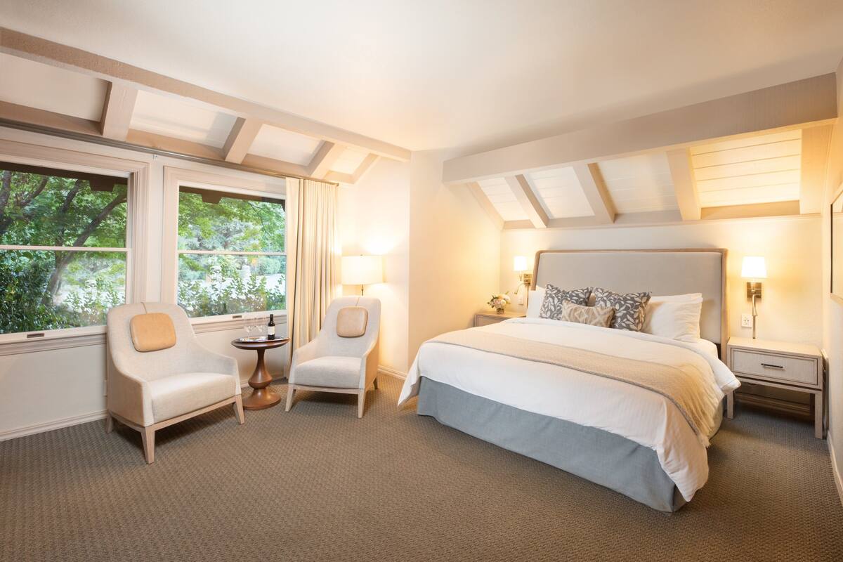 A hotel room with a large bed, two armchairs, a small table, and a nightstand.