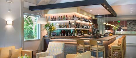 A bar area with a high ceiling and a variety of liquor bottles. There are several seating areas with patterned upholstery.