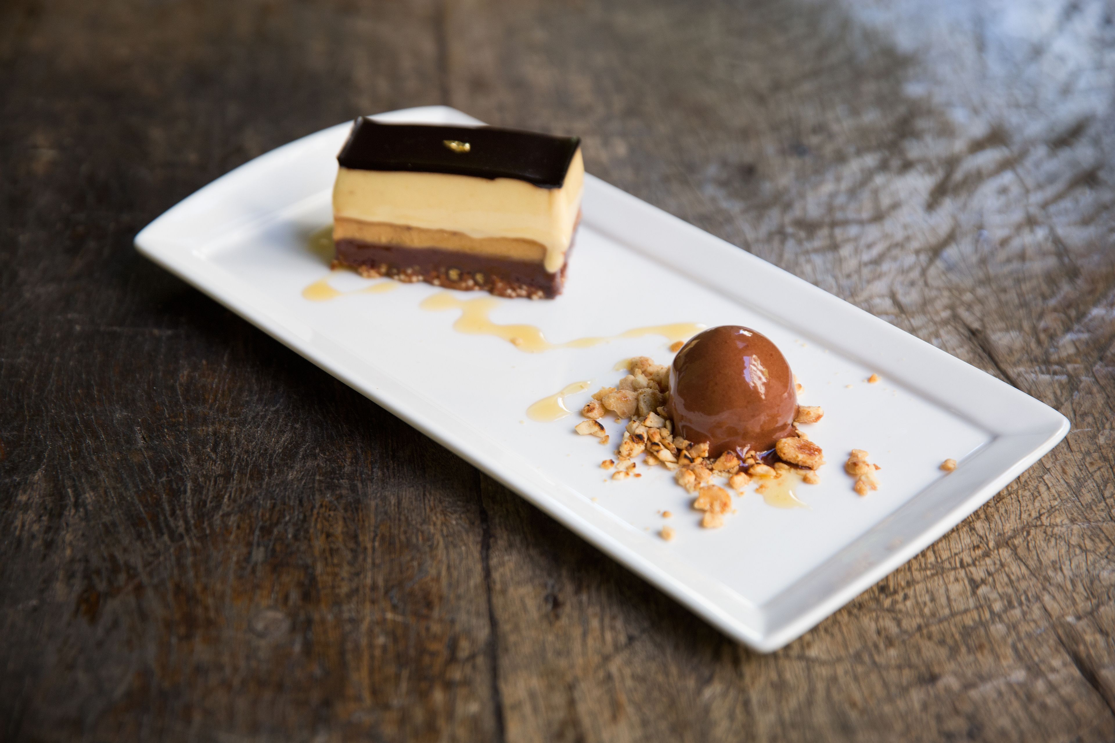 Un postre sobre un plato rectangular blanco con salsa de caramelo y nueces desmenuzadas sobre una superficie de madera.