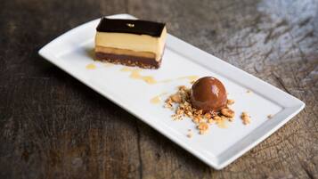Un postre sobre un plato rectangular blanco con salsa de caramelo y nueces desmenuzadas sobre una superficie de madera.