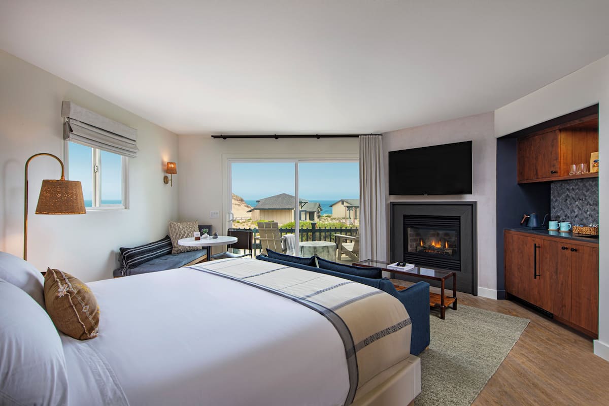 Quarto de hotel moderno com uma cama grande, lareira, televisão e vista para o oceano.