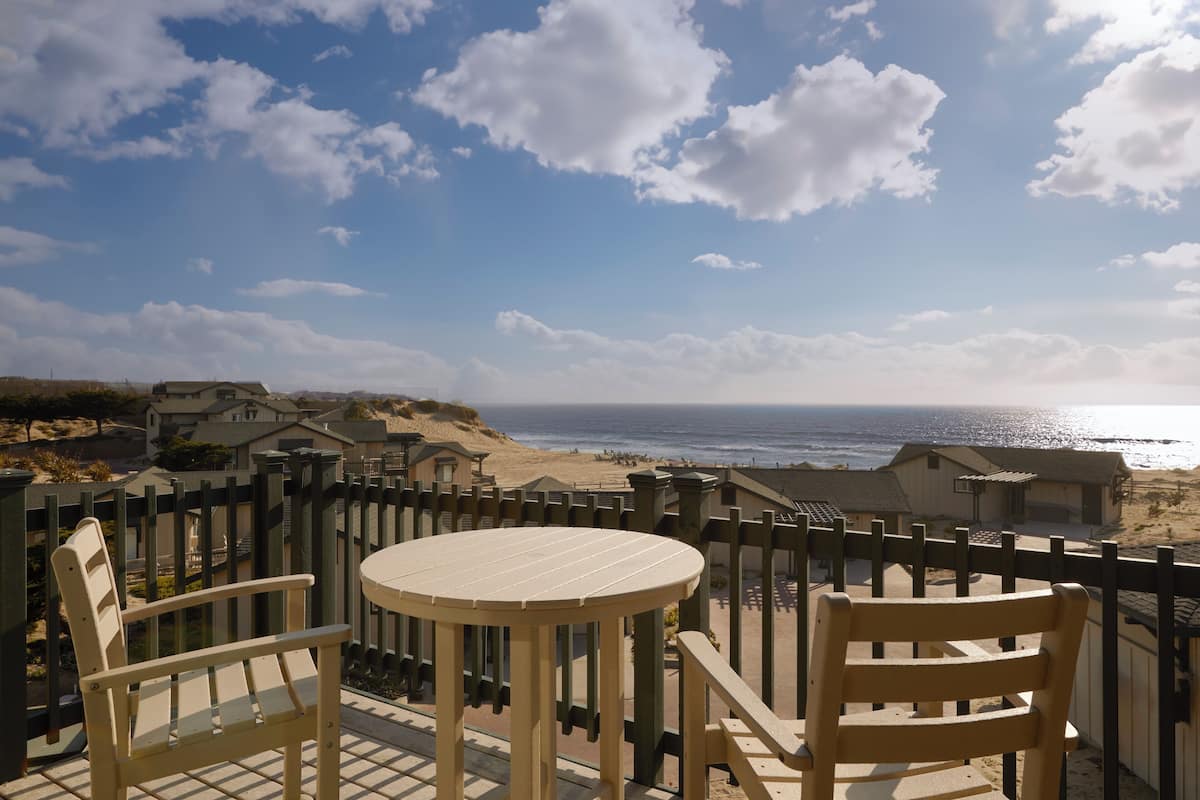 Varanda com mesa redonda e duas cadeiras, com vista para a praia e o oceano.