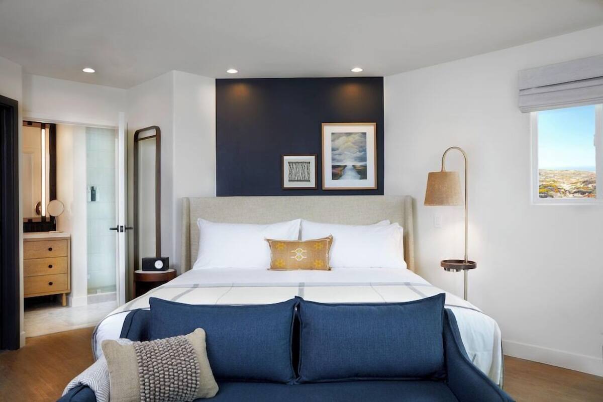 Een moderne slaapkamer met een groot bed, nachtkastjes, een spiegel en kunst aan de muur.