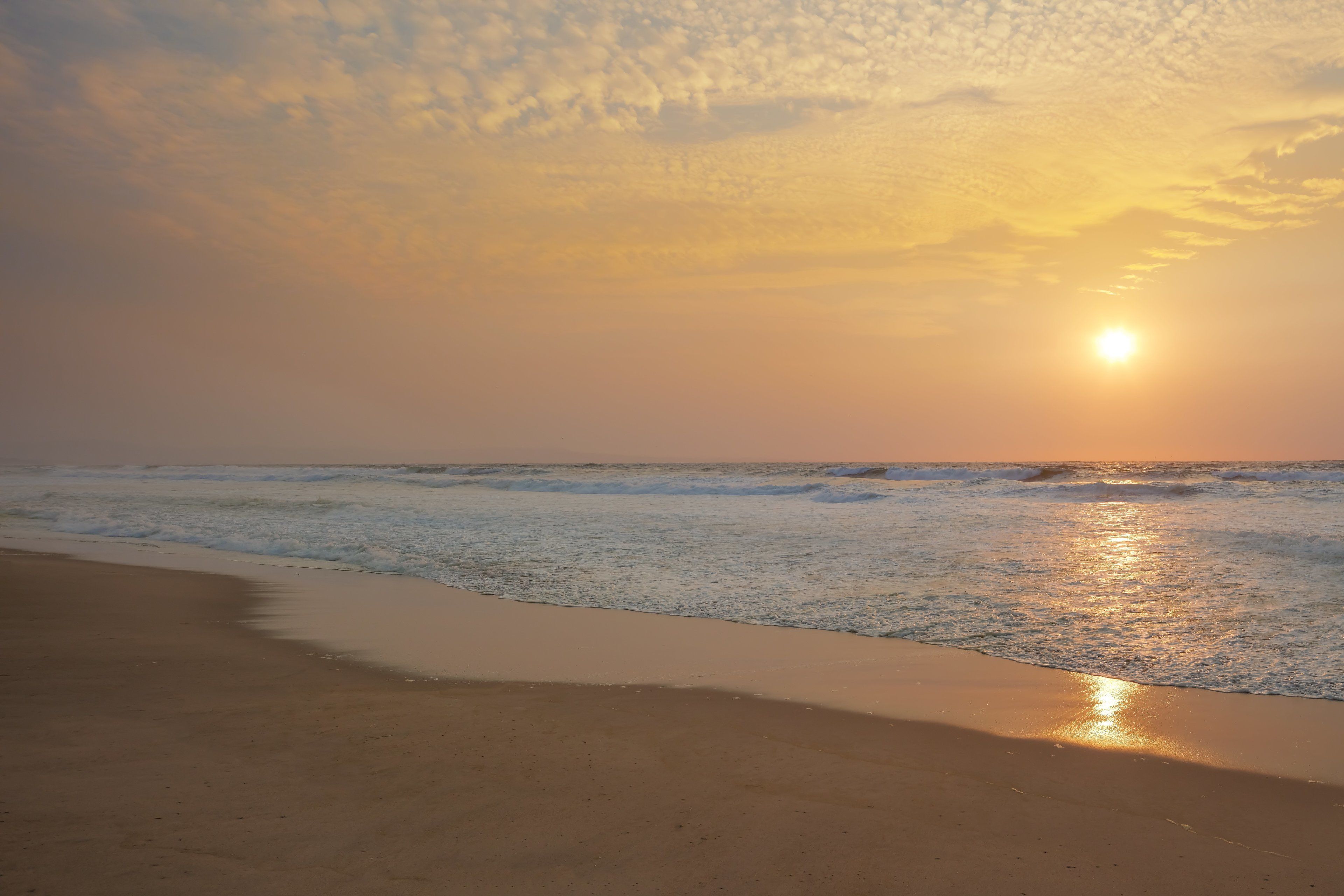 Uma praia com o pôr do sol sobre o oceano.
