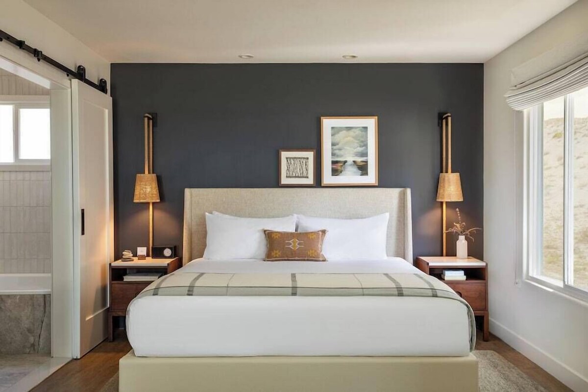 Un dormitorio con una cama grande, dos mesitas de noche, una pared oscura y una ventana.