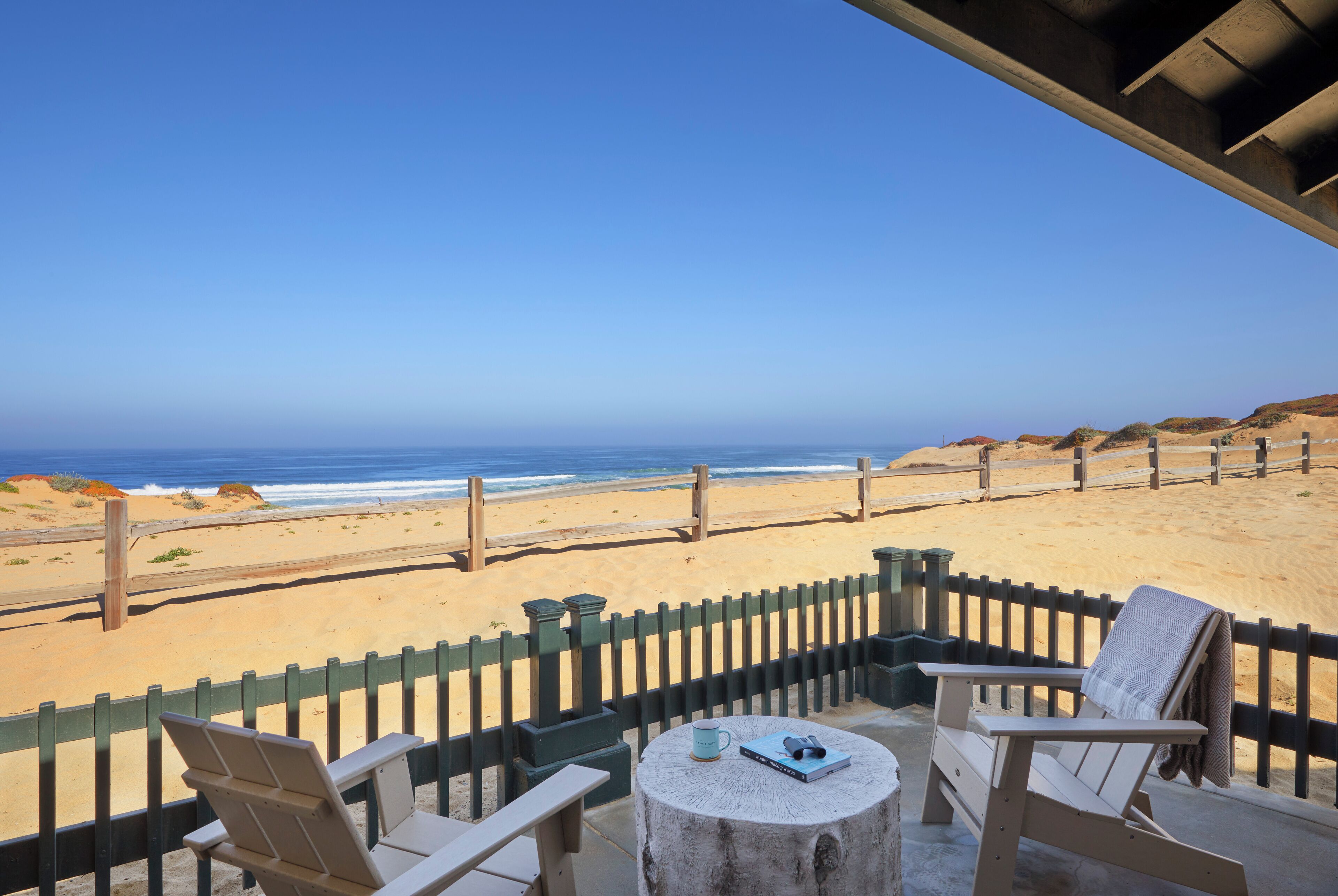 A beachside patio with two chairs and a table, overlooking the ocean.
