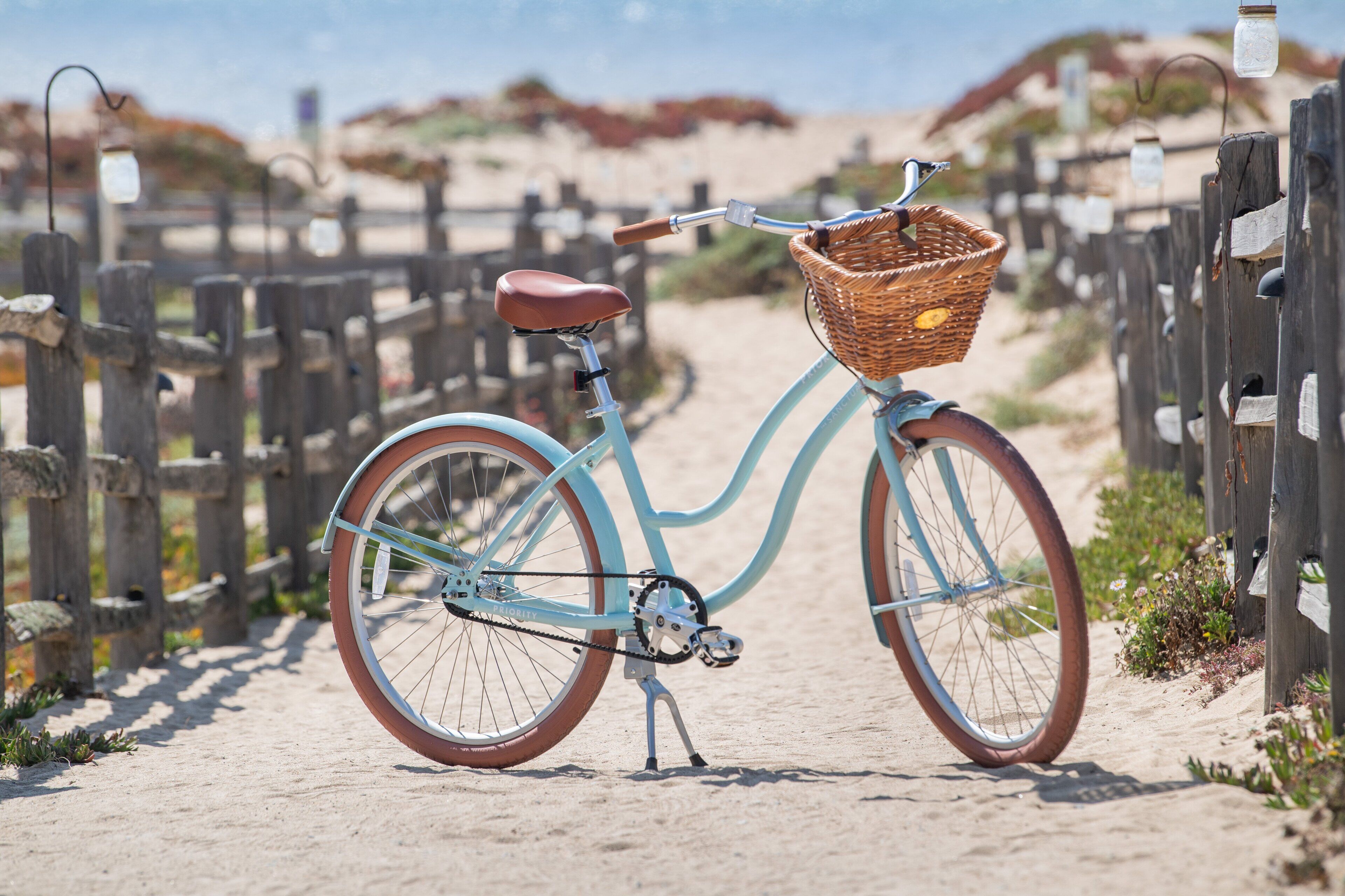 A bicycle with a wicker basket parked on a sandy path.