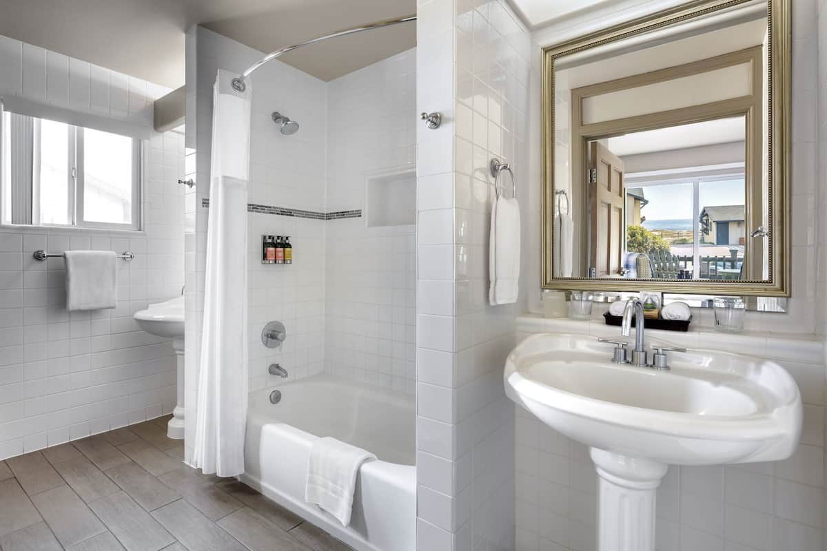 Casa de banho moderna com banheira, chuveiro e lavatório, tudo em branco.