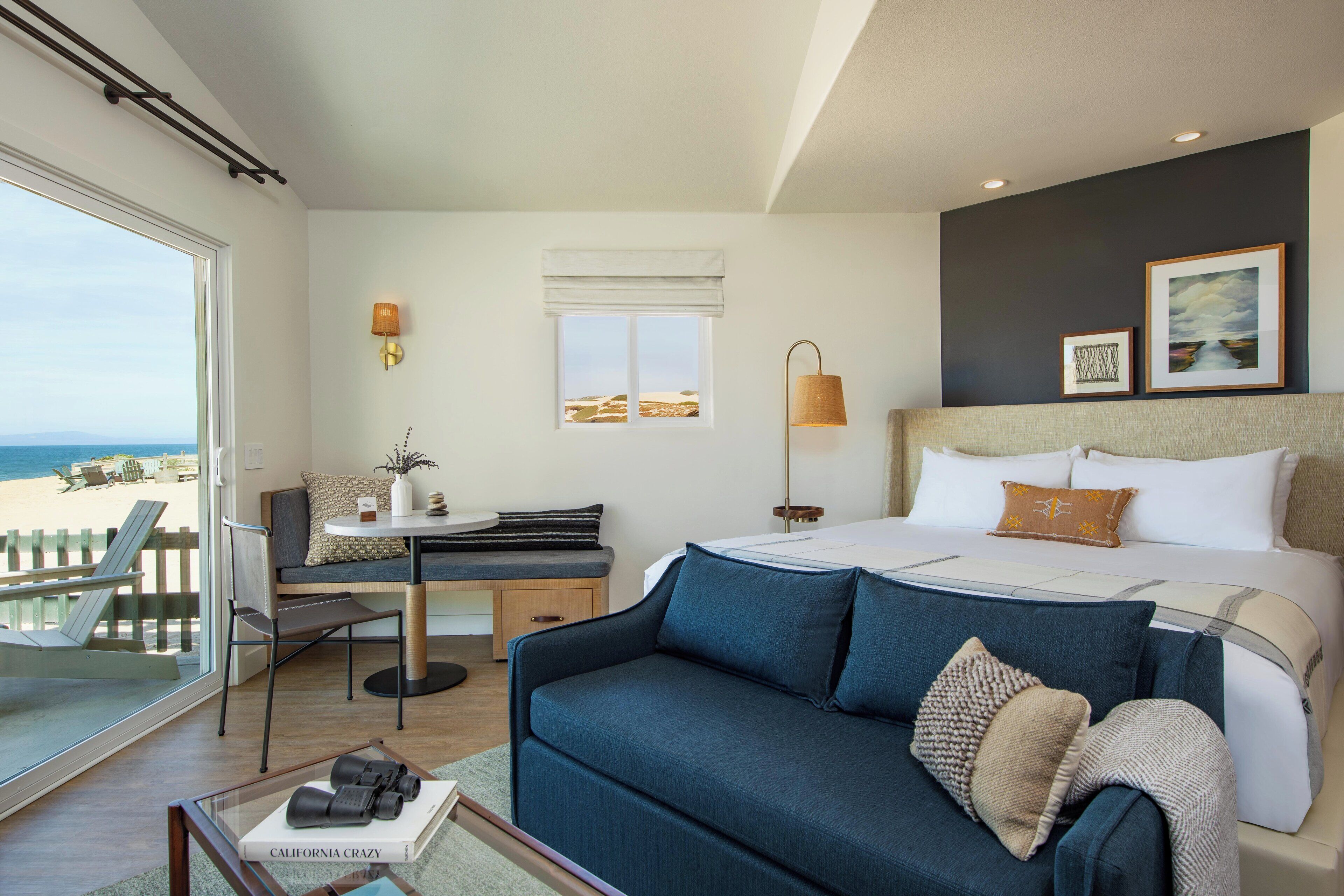 A hotel room with a bed, a sofa, a desk, and a view of the beach.