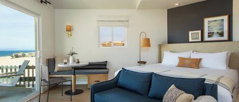A hotel room with a bed, a sofa, a desk, and a view of the beach.