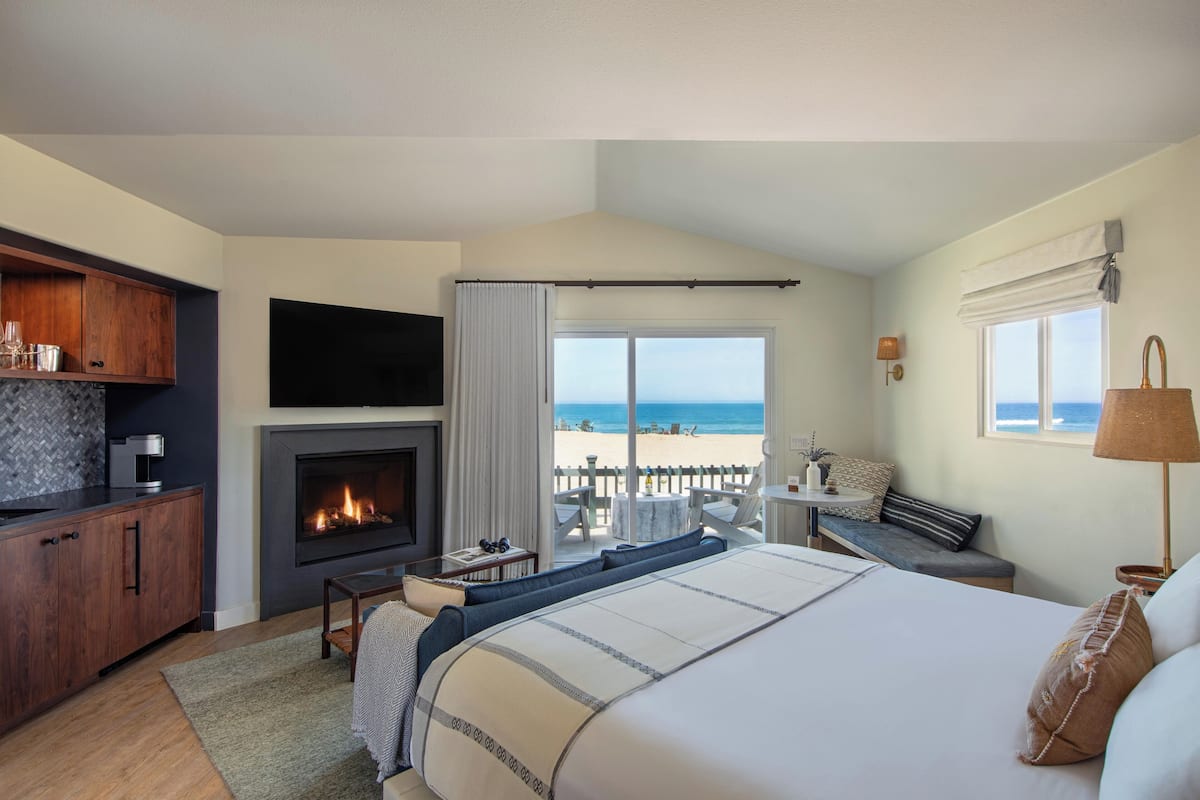 Quarto com cama grande, lareira, televisão, escrivaninha com cadeira e vista para a praia.