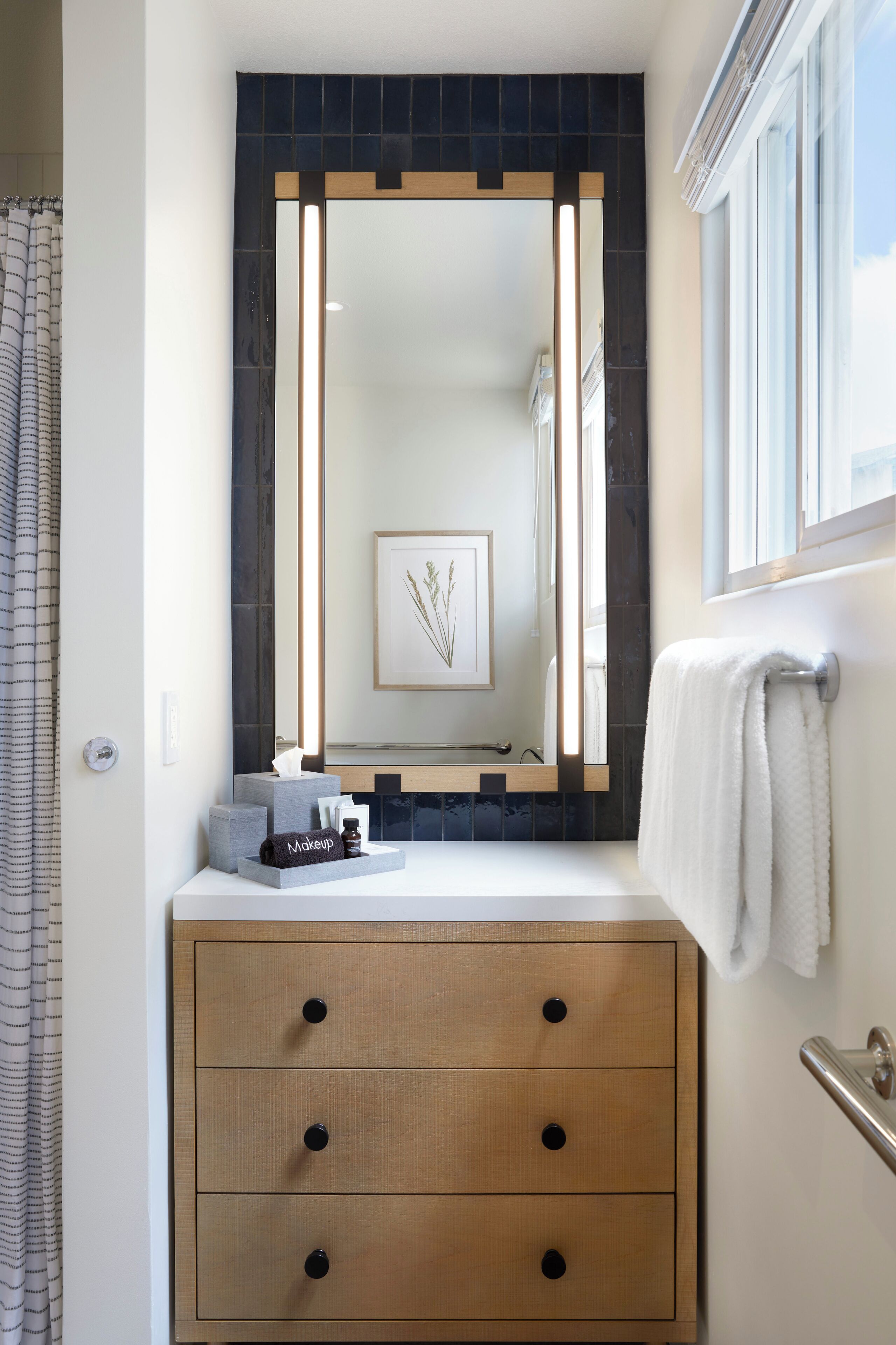 A bathroom with a large mirror, a wooden vanity, a towel rack, and a framed artwork on the wall.
