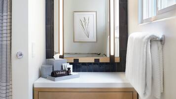 A bathroom with a large mirror, a wooden vanity, a towel rack, and a framed artwork on the wall.