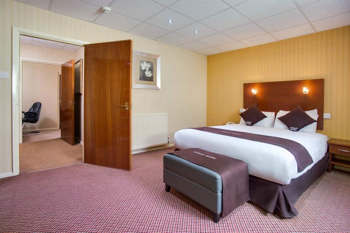 A hotel room with a large bed, a wooden headboard, a bedside table, and a chair.
