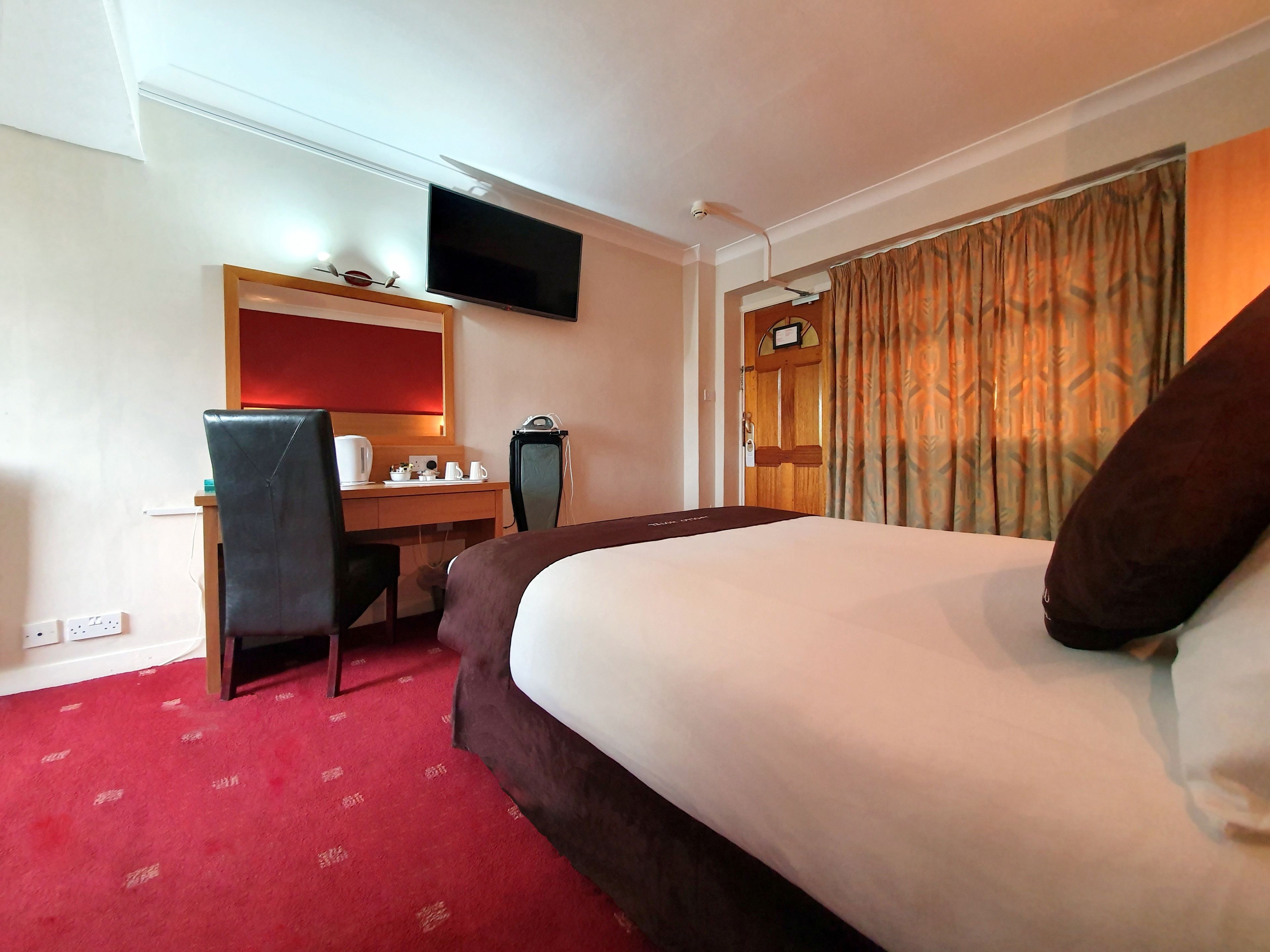 Une chambre d’hôtel comprenant un lit, un bureau avec une chaise, un téléviseur fixé au mur et une fenêtre avec des rideaux.