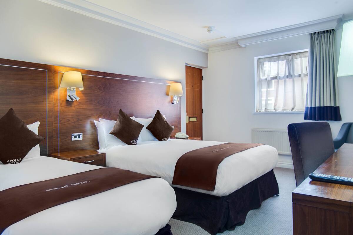 A hotel room with two beds, a desk, and a chair.