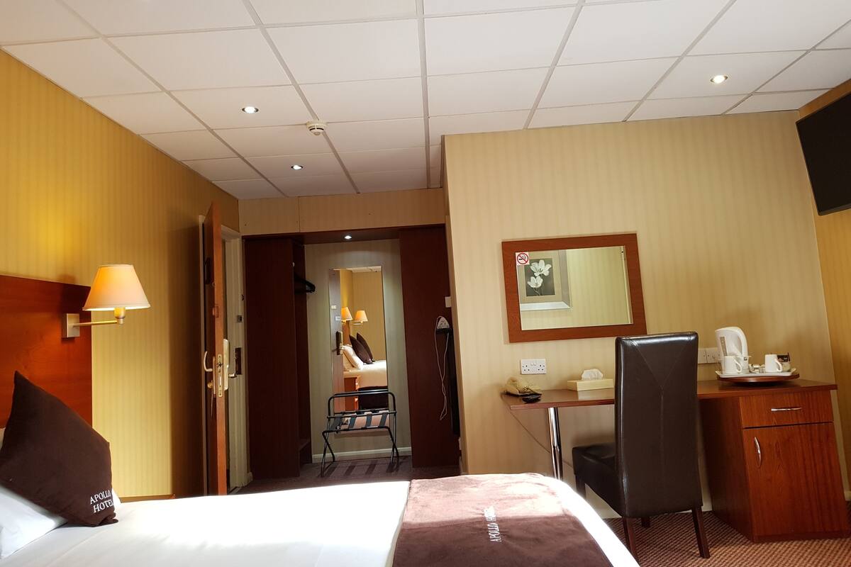 A hotel room with a bed, desk, chair, and a small kitchenette.