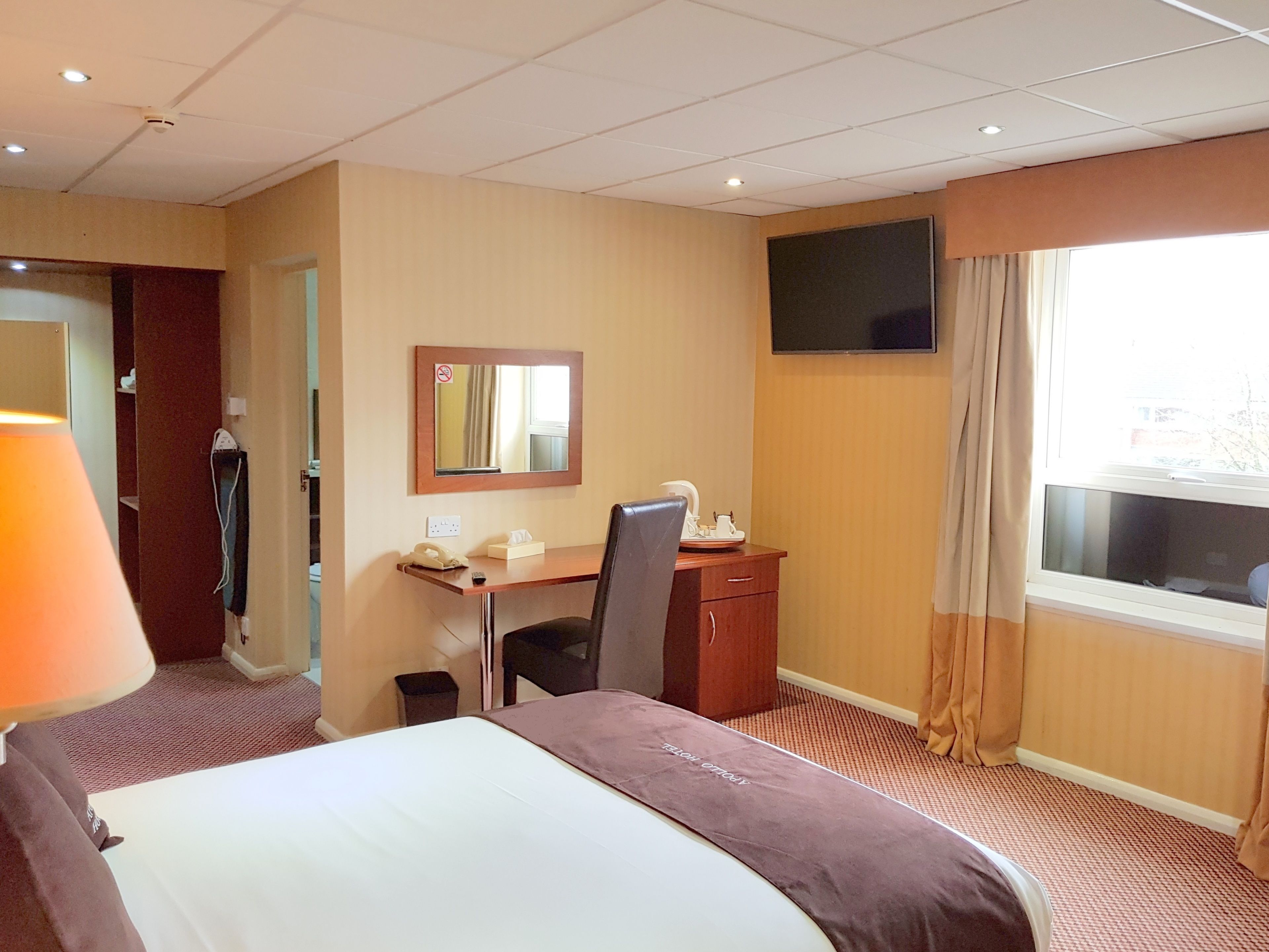 A hotel room with a bed, a desk, a chair, a television, and a window with curtains.