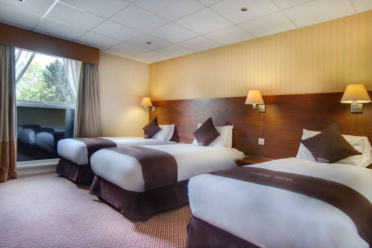A hotel room with two beds, a large window, and a view of trees.
