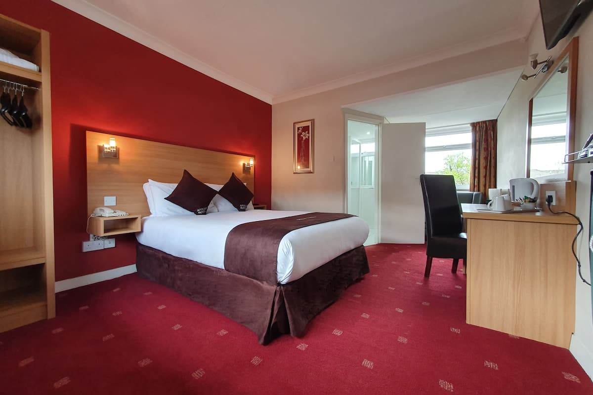 A hotel room with a large bed, a desk, a chair, a wardrobe, and a red carpet.