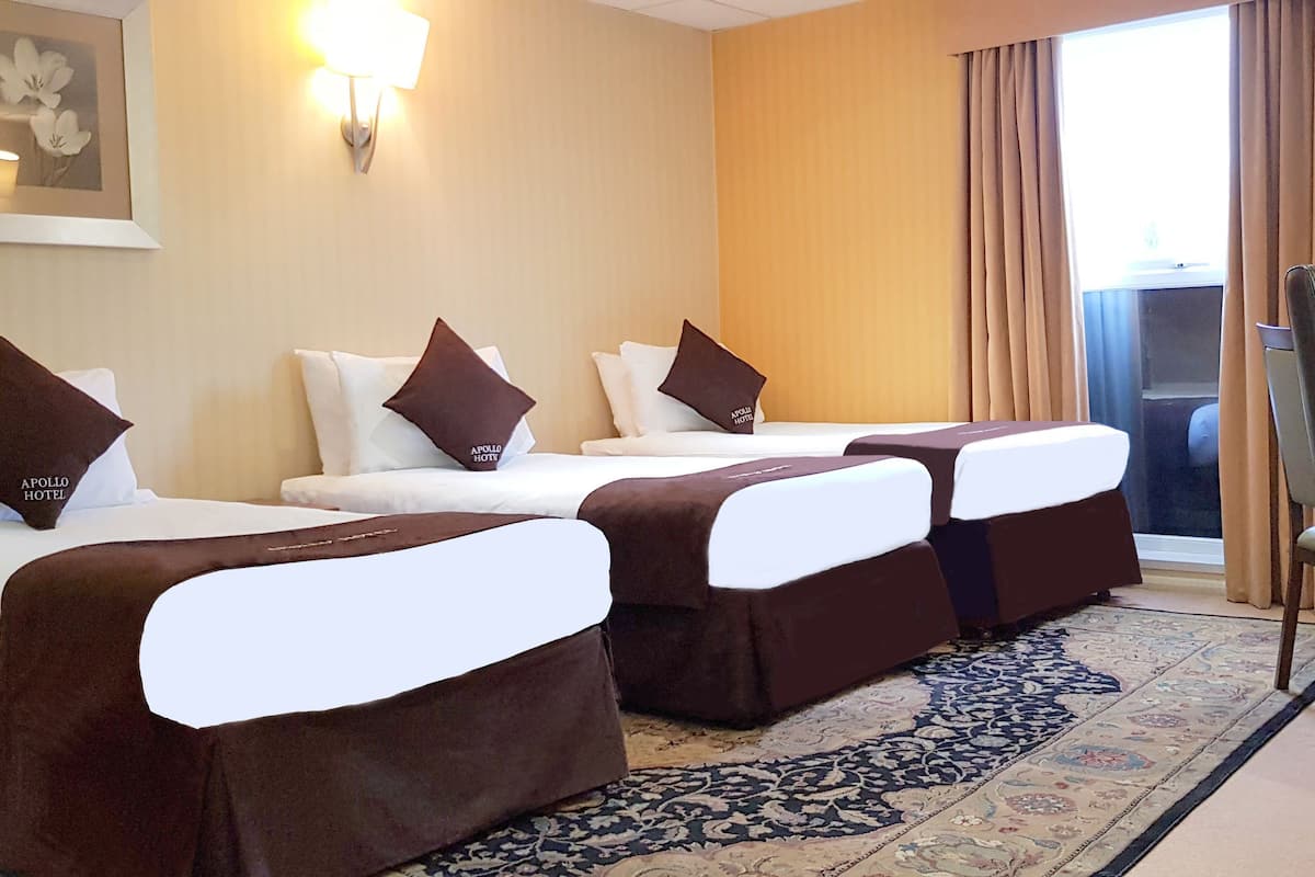 A hotel room with two single beds, a desk, a chair, and a large window with curtains.