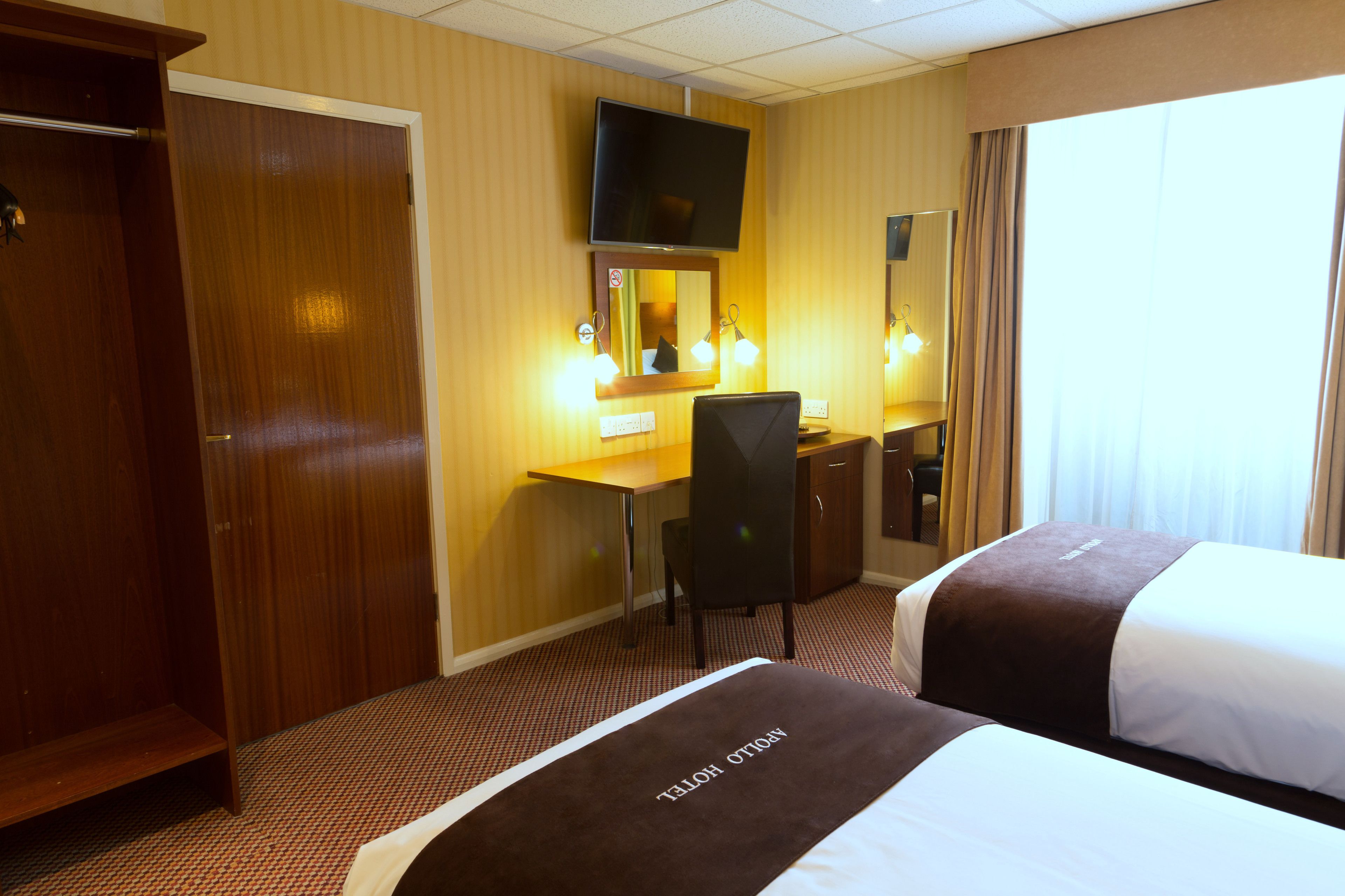 A hotel room with two beds, a desk, a chair, a TV, and a wardrobe.