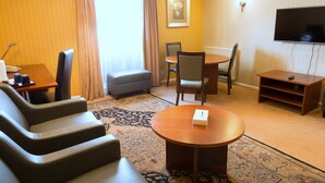 Una habitación de hotel con sofá, una mesa redonda, televisor y una mesita con control remoto.