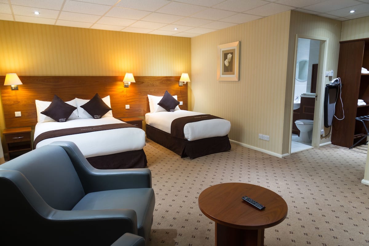A hotel room with two beds, a sofa, a round table, and a bathroom visible through an open door.