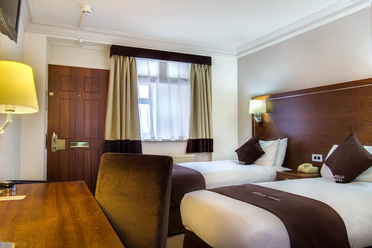 A hotel room with two beds, a wooden desk, and a chair.