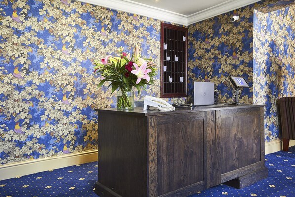 Een receptiebalie met een telefoon, een vaas met bloemen en een raam met roeders.