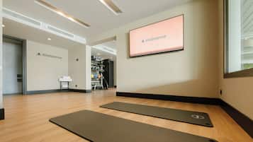 A WeBalance studio with exercise mats, a TV screen, and a view of the gym area.