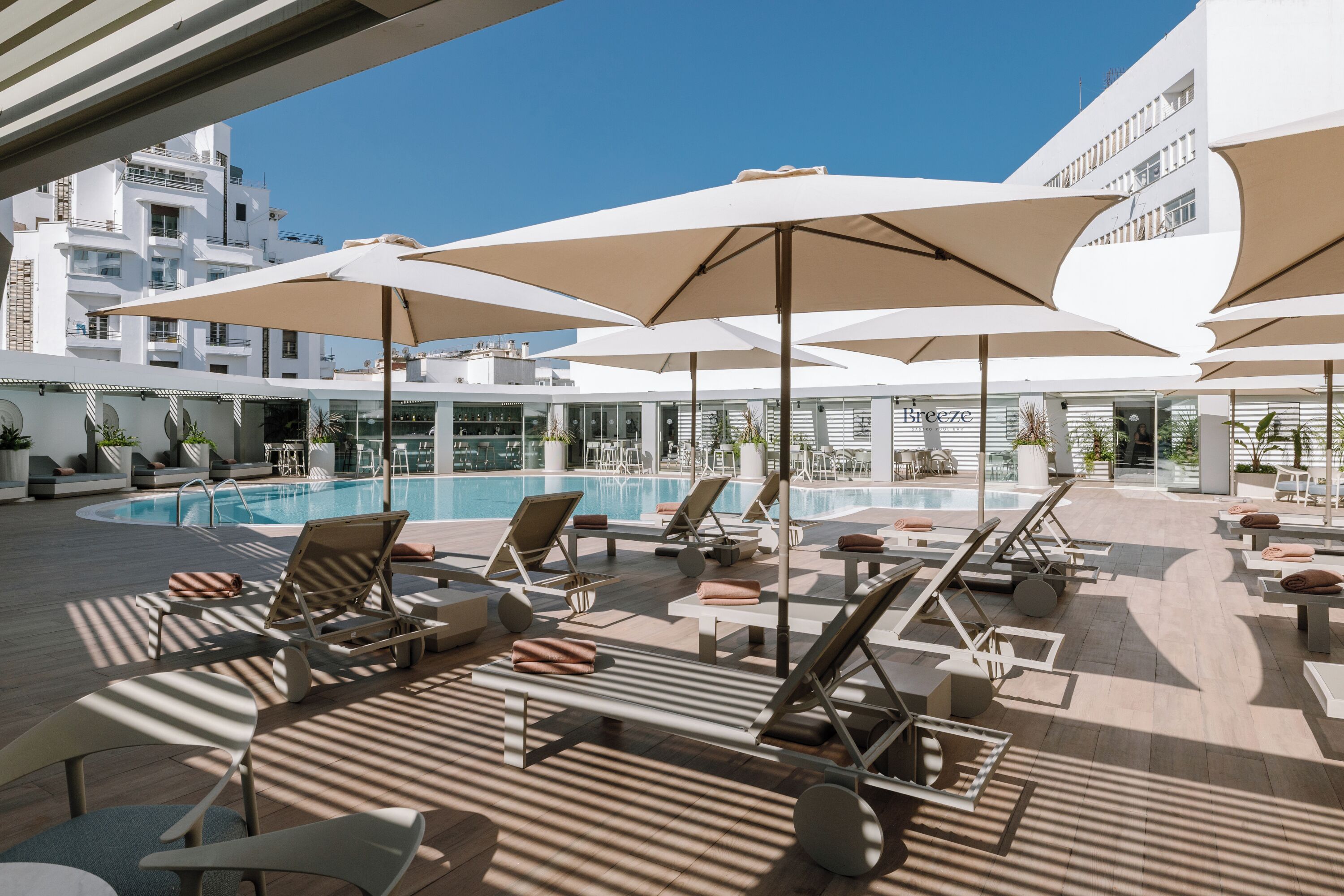 Un espace piscine aménagé sur le toit, avec des chaises longues, des parasols et une vue dégagée sur les bâtiments environnants.