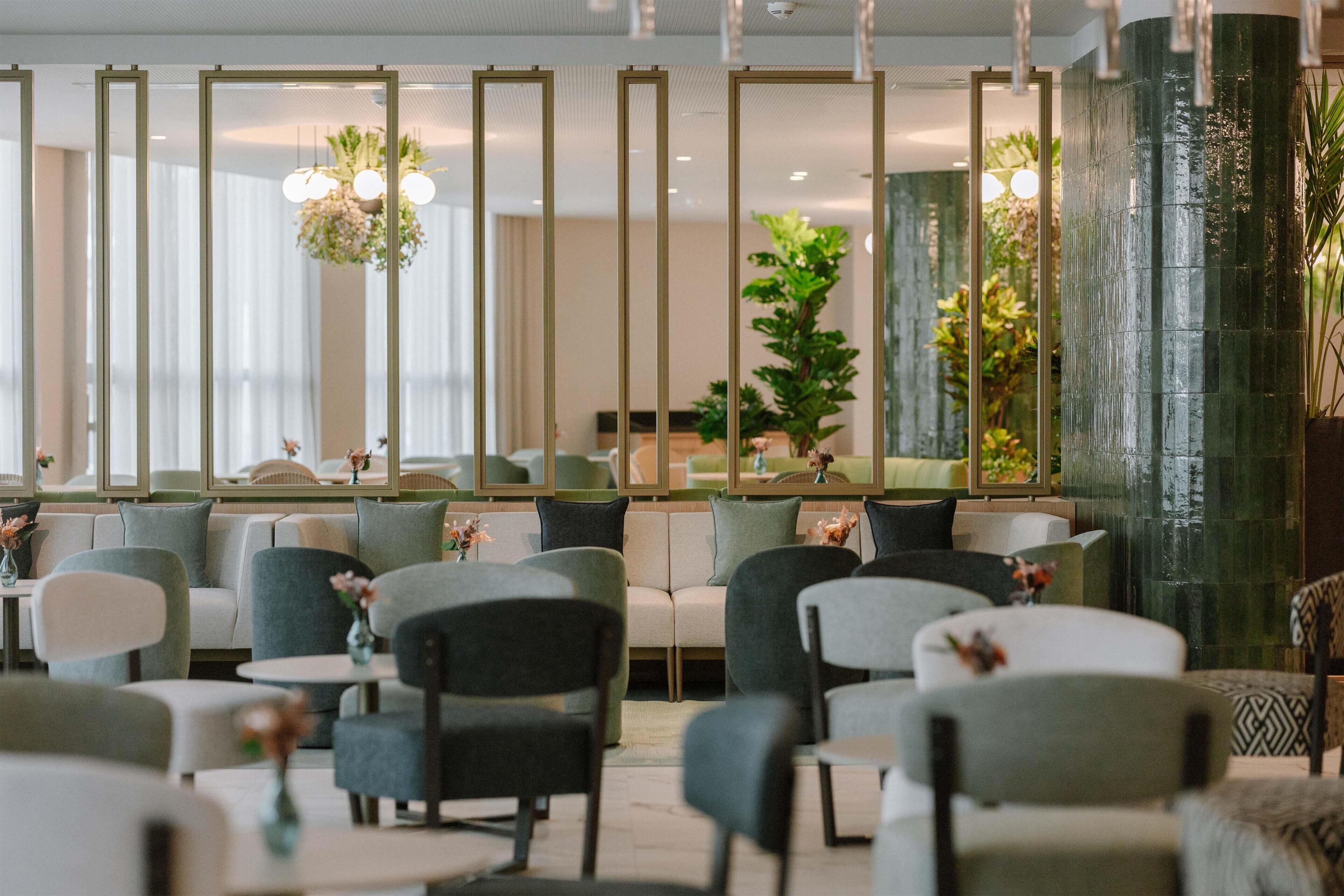 Una hall d'albergo moderna con aree salotto, una reception e piante ornamentali.