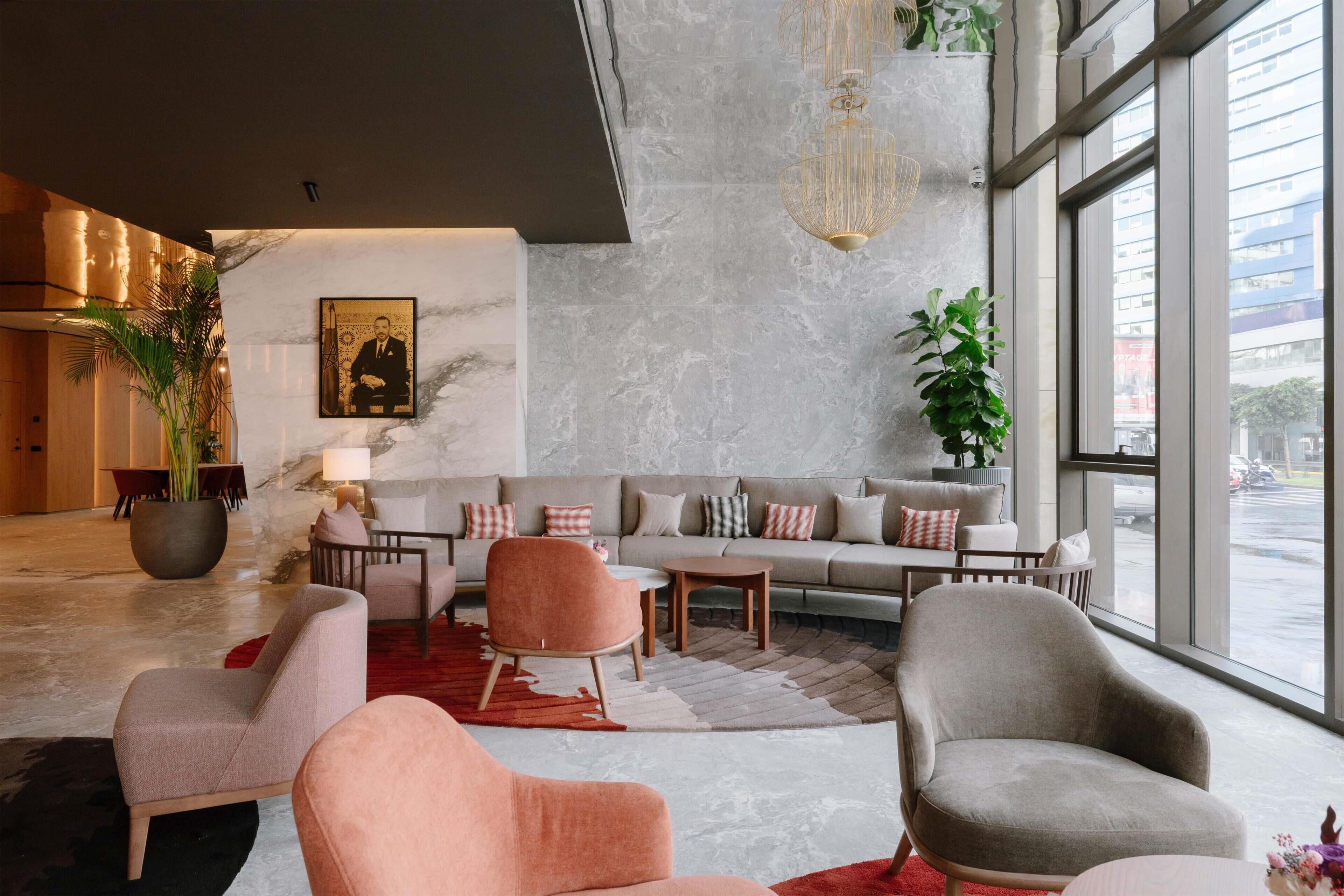 A modern lobby with a marble wall, a large plant, a sofa set, and a view through large windows.