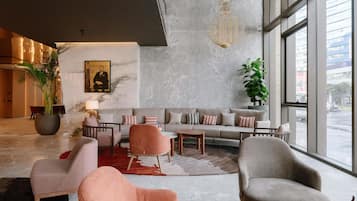 A modern lobby with a marble wall, a large plant, a sofa set, and a view through large windows.