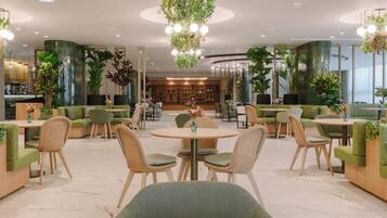 Ein moderner Lounge-Bereich mit grünen Sitzgelegenheiten, runden Tischen und hängenden Pflanzen.