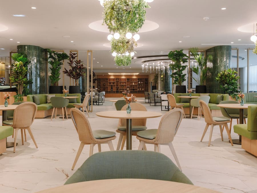 Ein moderner Lounge-Bereich mit grünen Sitzgelegenheiten, runden Tischen und hängenden Pflanzen.