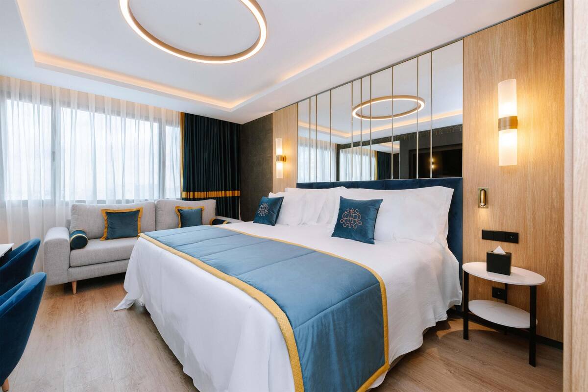 A modern hotel room with a large bed, a sofa, a small table, and a mirror.