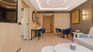 A modern hotel room with a dining area, a sofa, and a TV.